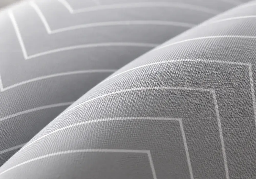 Close-up of the pillow’s grey fabric with fine white herringbone, raking light showing the weave